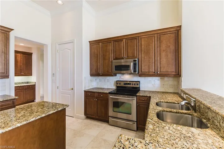 Kitchen with appliances with stainless steel finishes, ornamental molding, light stone countertops, decorative backsplash, and light tile patterned floors