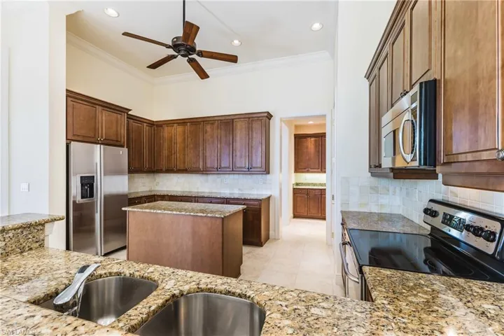 Kitchen featuring stainless steel appliances, ornamental molding, light stone countertops, decorative backsplash, and light tile patterned floors