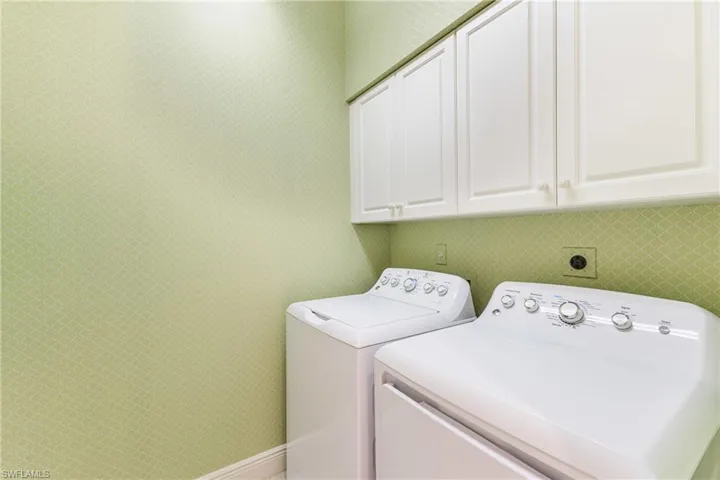 Laundry room with washing machine and dryer, wallpapered walls, and cabinet space