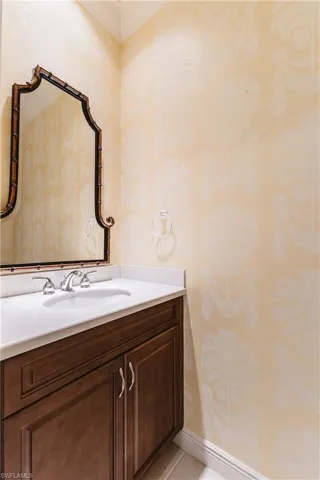 Bathroom with wallpapered walls, vanity, crown molding, and light tile patterned floors