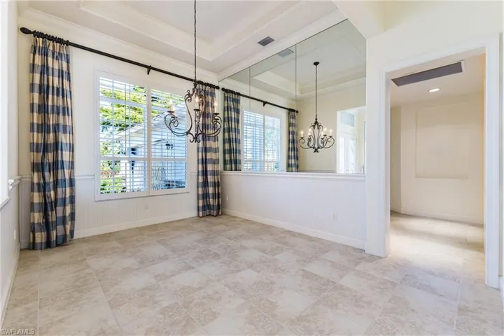 Unfurnished dining area featuring a chandelier, a raised ceiling, ornamental molding, and wainscoting