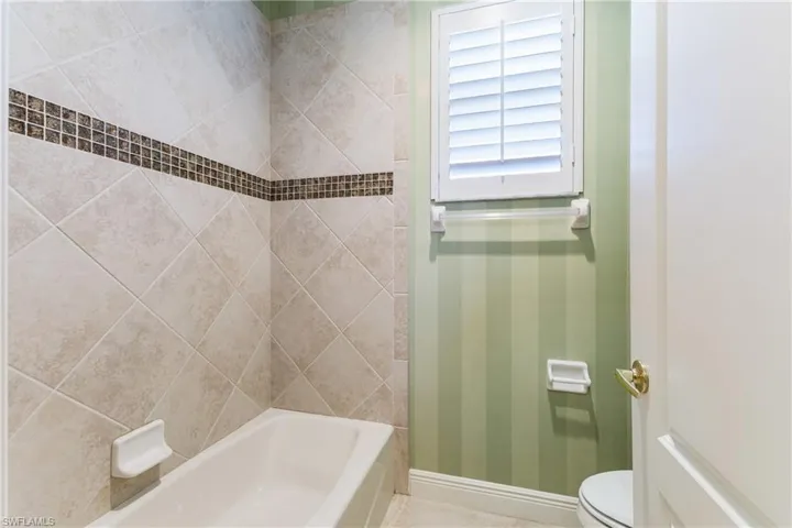 Full bathroom with wallpapered walls and shower / bath combination