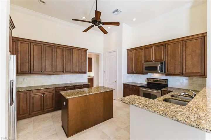 Kitchen with stainless steel appliances, light stone counters, crown molding, backsplash, and a kitchen island