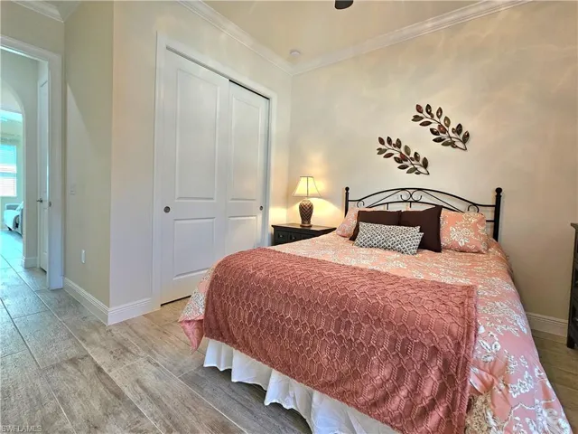 Bedroom featuring light wood-style tile flooring, a closet, baseboards, and crown molding