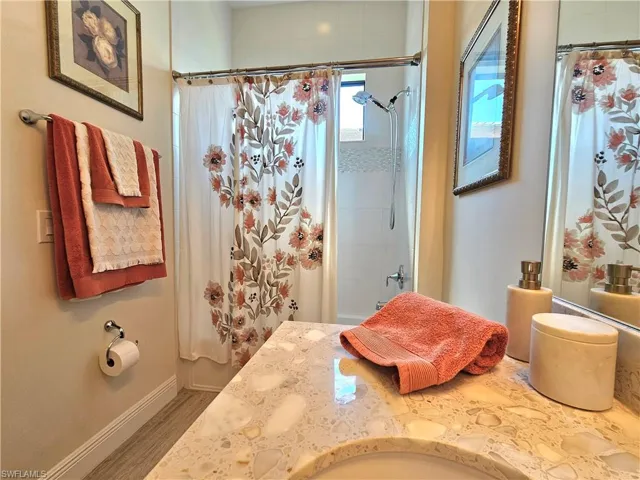 Bathroom with shower / bath combination with curtain, vanity, baseboards, and wood like tile finished floors