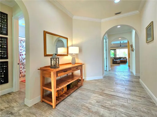 Hall with arched walkways, wood like tile finished floors, and ornamental molding