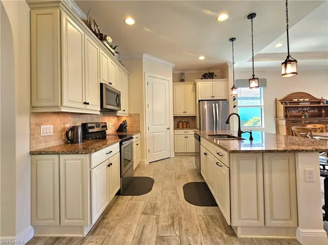 Kitchen featuring light tile floors, appliances with stainless steel finishes, a sink, and crown molding