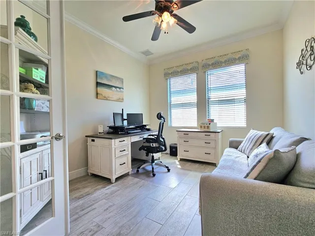 Office space with light tile floors, visible vents, crown molding, and a ceiling fan
