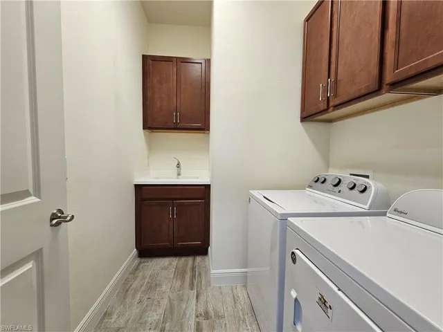 Laundry area featuring cabinet space, washing machine and dryer, light tile floors, and a sink