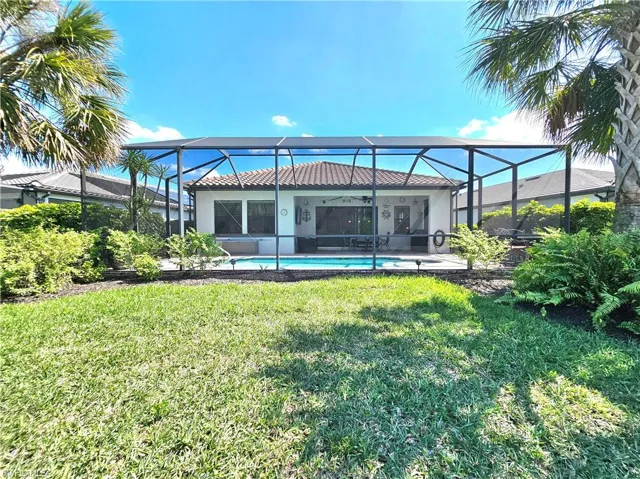Back of house with a lanai, an outdoor pool, a tile roof, a yard, and stucco siding