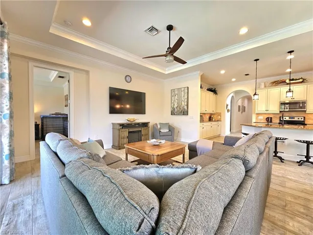Living area featuring light tile floors, visible vents, arched walkways, a ceiling fan, and ornamental molding