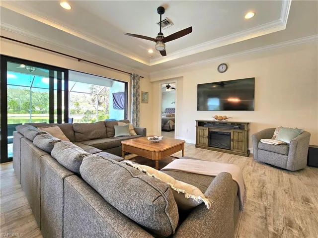 Living room featuring visible vents, a glass covered fireplace, a tray ceiling, crown molding, and light tile floors