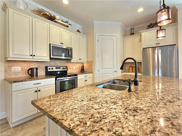 Kitchen featuring decorative backsplash, appliances with stainless steel finishes, light stone countertops, crown molding, and a sink