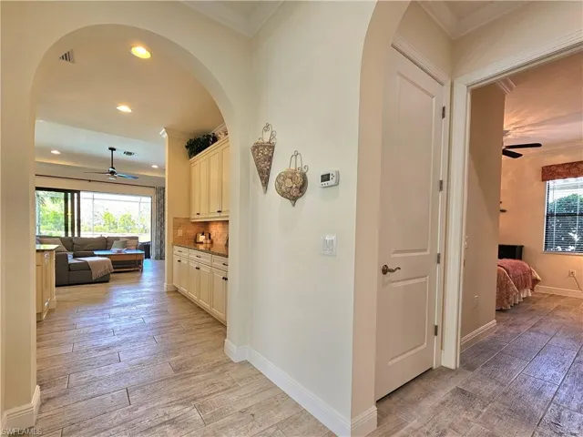 Corridor with light wood like tile finished floors, baseboards, arched walkways, and crown molding