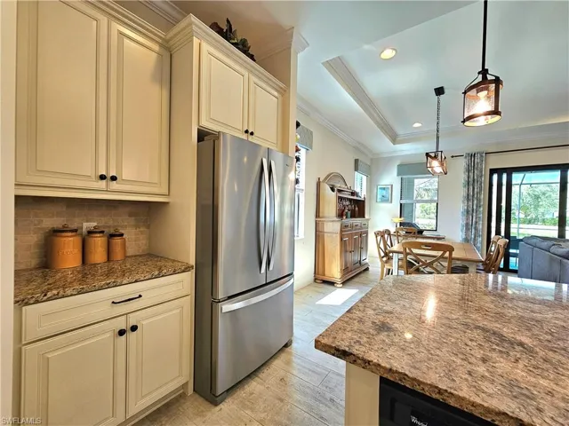 Kitchen featuring dark stone countertops, freestanding refrigerator, a tray ceiling, crown molding, and cream cabinetry