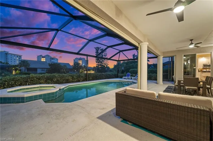 Pool at dusk with ceiling fan, a patio, an in ground hot tub, an outdoor hangout area, and glass enclosure
