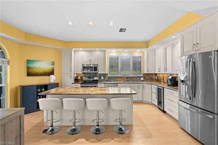 Kitchen featuring decorative backsplash, beverage cooler, stainless steel appliances, and white cabinets