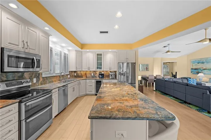 Kitchen featuring tasteful backsplash, ceiling fan, stainless steel appliances, wine cooler, and a kitchen island