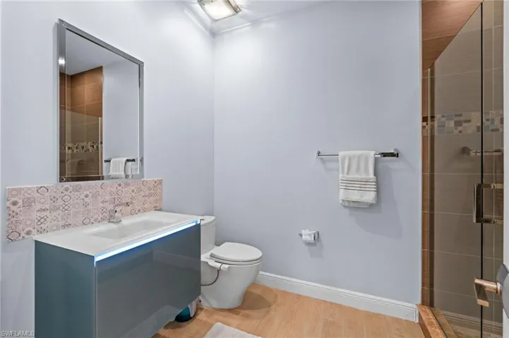 Bathroom featuring vanity, tasteful backsplash, hardwood / wood-style flooring, walk in shower, and toilet