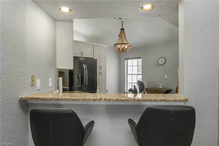 Kitchen featuring a textured wall, a textured ceiling, light stone counters, stainless steel refrigerator with ice dispenser, and pendant lighting