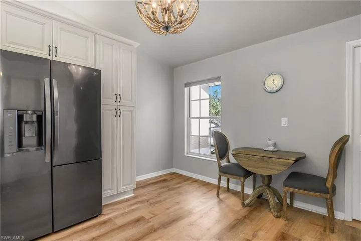 Kitchen featuring stainless steel fridge, light wood-style flooring, a chandelier, white cabinetry, and decorative light fixtures