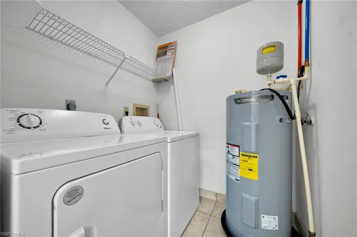 Laundry room featuring water heater, light tile patterned flooring, a textured ceiling, and independent washer and dryer