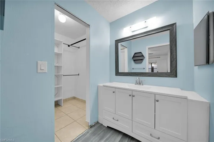 Bathroom with vanity, light tile patterned flooring, a textured ceiling, and a spacious closet