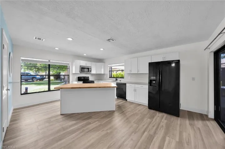 Kitchen featuring white cabinetry, black appliances, a kitchen island, wood counters, and a textured ceiling