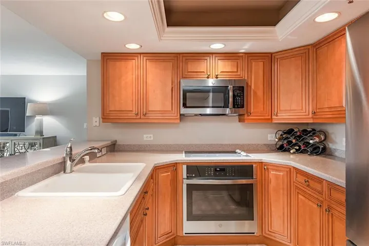 Kitchen with appliances with stainless steel finishes, recessed lighting, brown cabinetry, and a raised ceiling