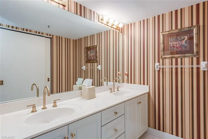 Full bath with wallpapered walls, double vanity, and light tile patterned floors and stall shower