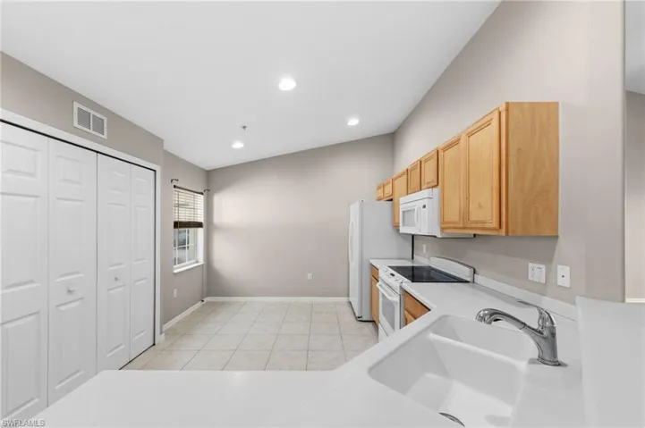 Kitchen area featuring a white sink, chrome faucet, white countertops, and light wood cabinetry