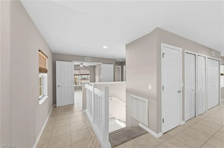 Upper-level landing featuring neutral-toned walls, tile flooring, white panel doors, and a staircase with white railings