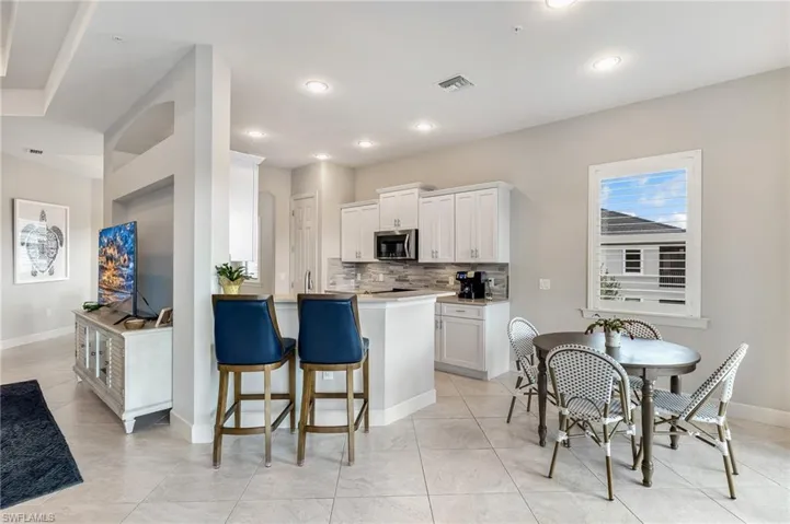 Kitchen featuring white cabinets, light countertops, a breakfast bar, decorative backsplash, and stainless steel microwave