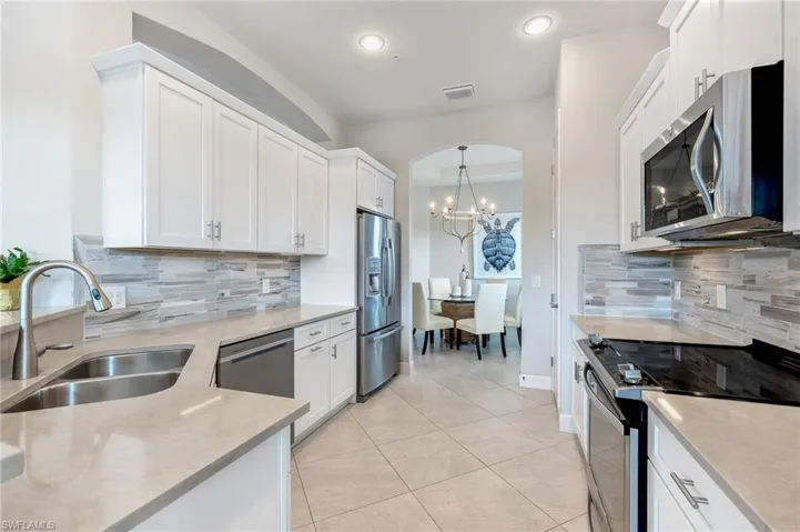 Kitchen with white cabinets, stainless steel appliances, light stone countertops, light tile patterned floors, and a chandelier