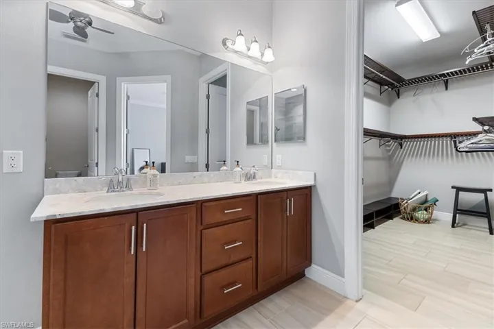 Bathroom featuring double vanity, baseboards, a walk in closet, and a ceiling fan