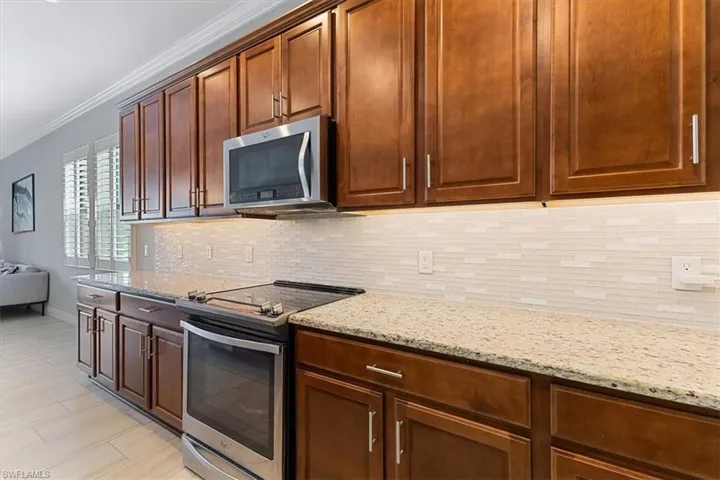 Kitchen featuring appliances with stainless steel finishes, ornamental molding, tasteful backsplash, light stone countertops, and baseboards