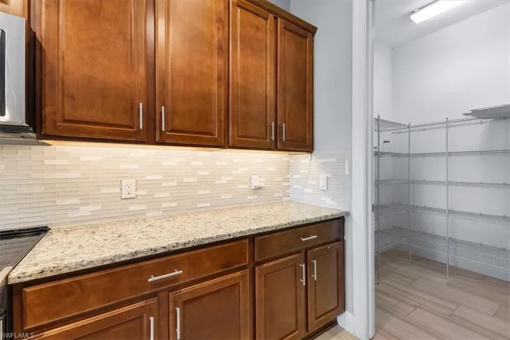 Kitchen with light stone counters, tasteful backsplash, stainless steel microwave, and light wood-style flooring