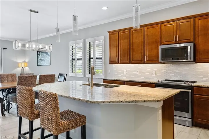 Kitchen featuring appliances with stainless steel finishes, a sink, backsplash, light stone countertops, and a center island with sink
