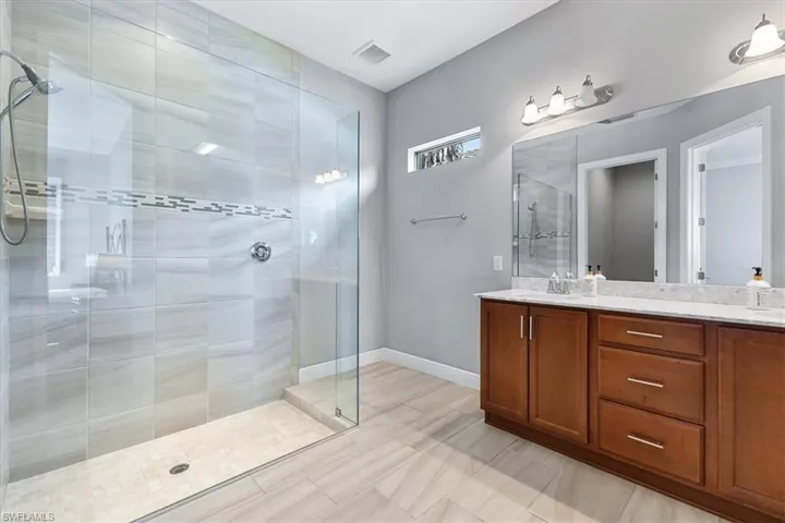 Bathroom with tiled shower, double vanity, baseboards, and tile patterned floors