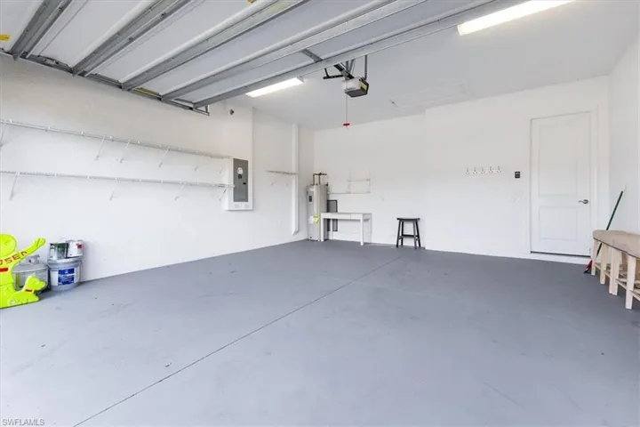 Garage with water heater, electric panel, and a garage door opener