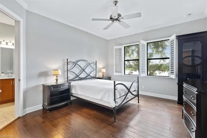 Bedroom featuring hardwood / wood-style floors, baseboards, ornamental molding, ensuite bathroom, and a ceiling fan