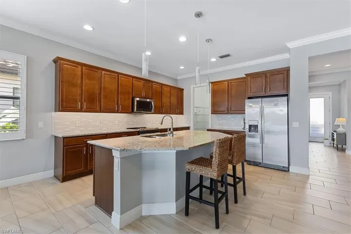 Kitchen with stainless steel appliances, a sink, backsplash, light stone countertops, and an island with sink