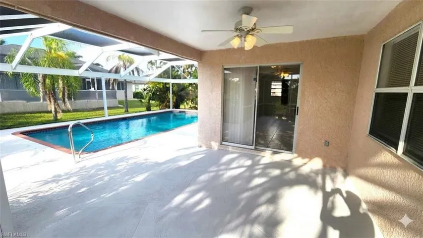 Screened outdoor living area featuring a rectangular pool with a handrail, an expansive patio, and a ceiling fan