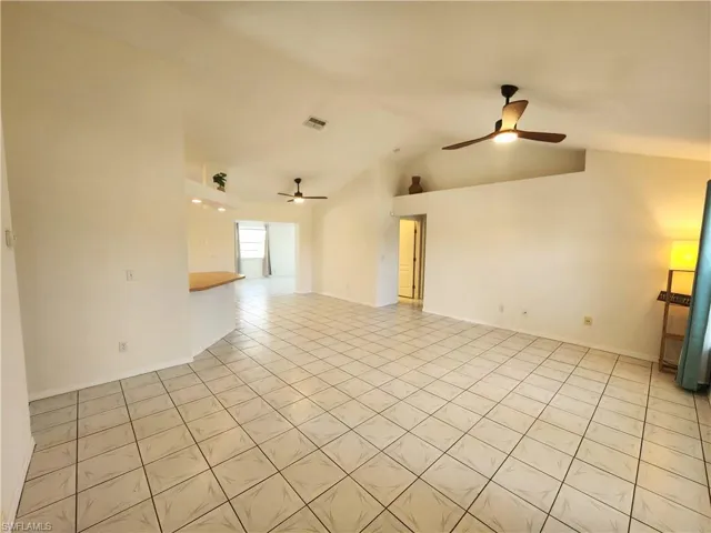 Spacious living area featuring diagonal tile flooring, vaulted ceilings, and two ceiling fans with integrated lighting
