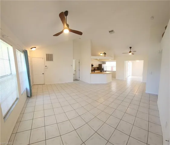 Spacious living area featuring light-toned tile flooring, vaulted ceilings, and multiple windows with blinds