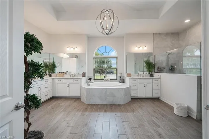 Full bath with a walk in shower, a garden tub, light wood-style flooring, and two vanities