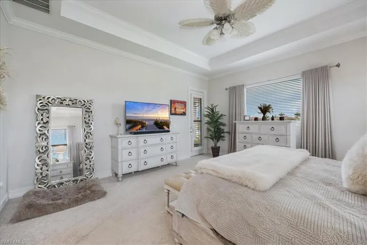 Bedroom with a tray ceiling, crown molding, light colored carpet, access to exterior, and a ceiling fan