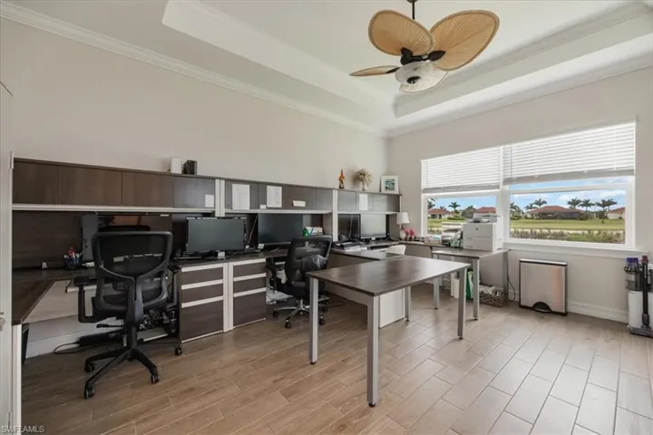 Home office with a tray ceiling, crown molding, light wood-type flooring, and ceiling fan