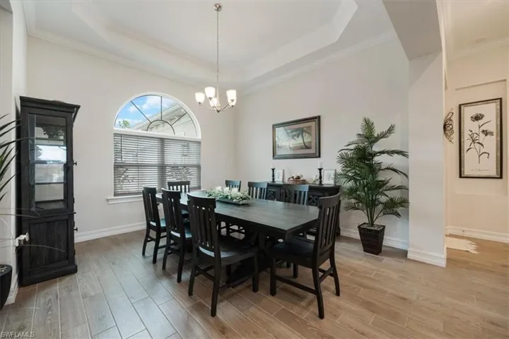 Dining room with a raised ceiling, light wood finished floors, ornamental molding, and a chandelier