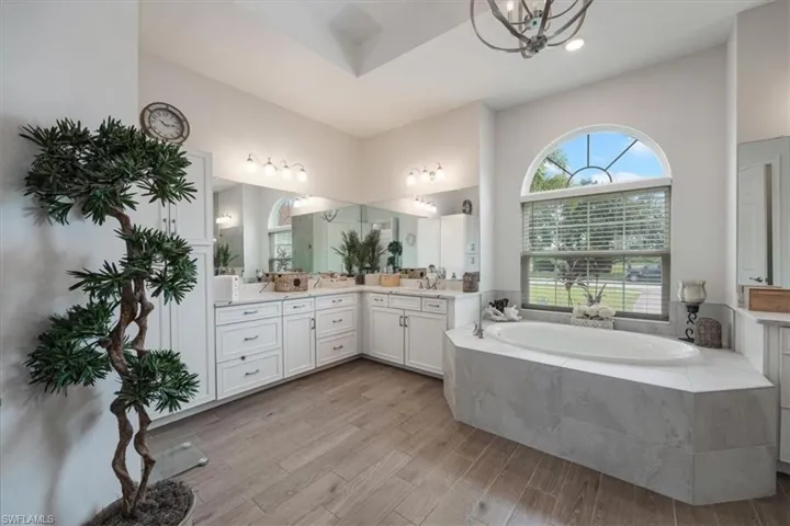 Bathroom featuring a bath, vanity, light wood finished floors, and a chandelier